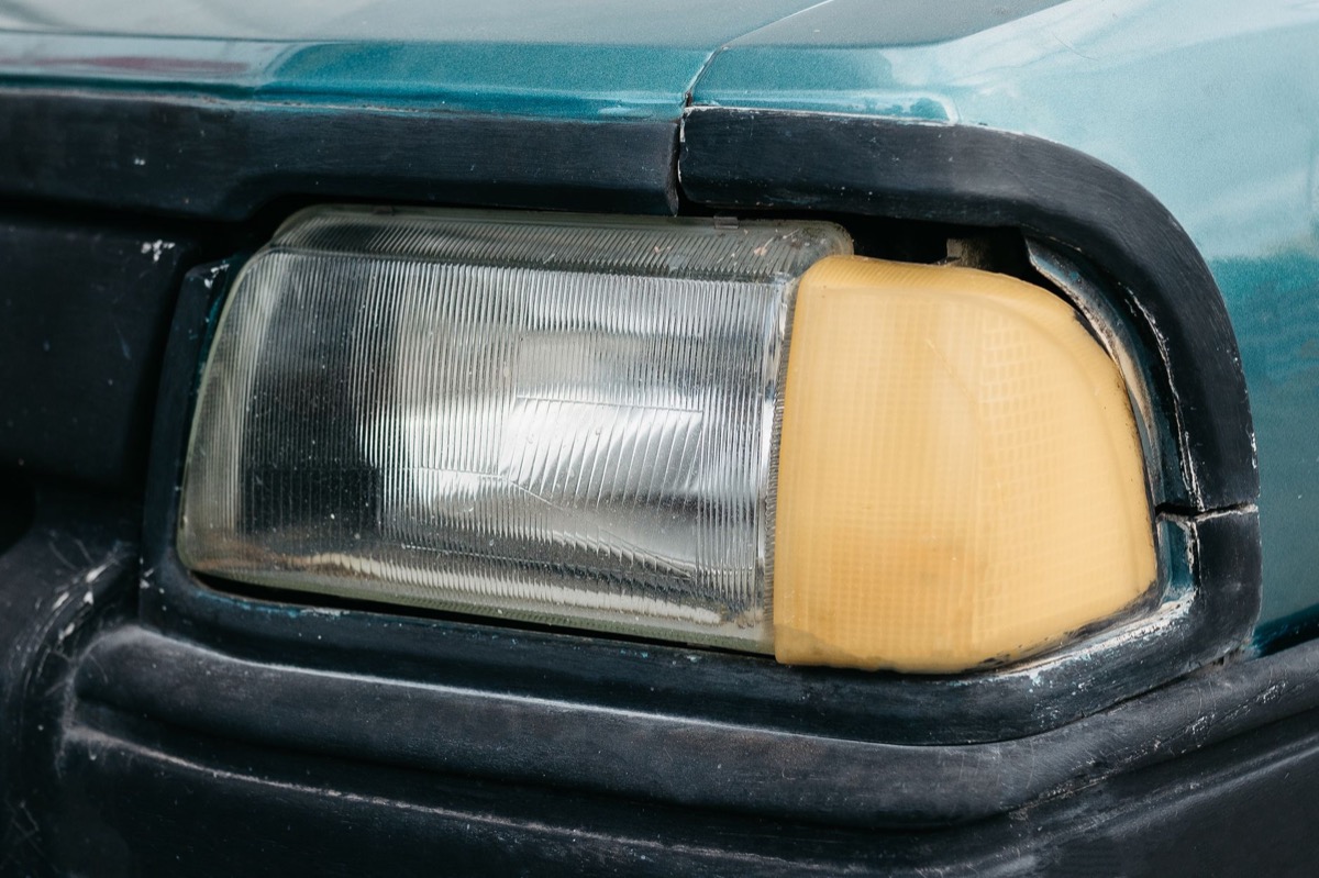 Detailed close-up of a person's hands carefully sanding peeling paint on a car's fender, preparing for repair.