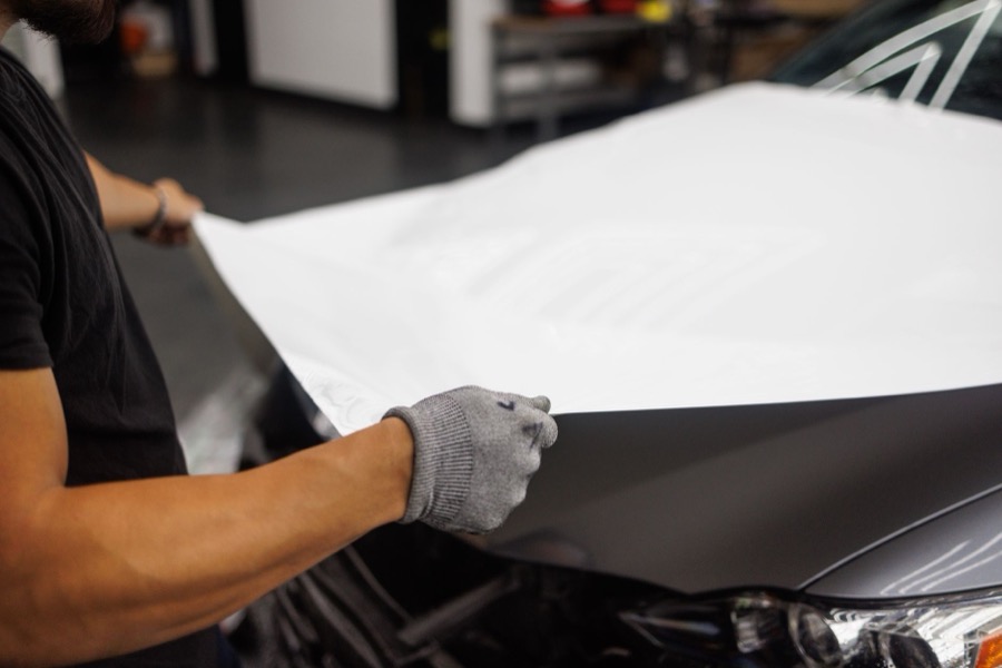 Close-up of a hand applying automotive primer to a prepped, repaired car surface.