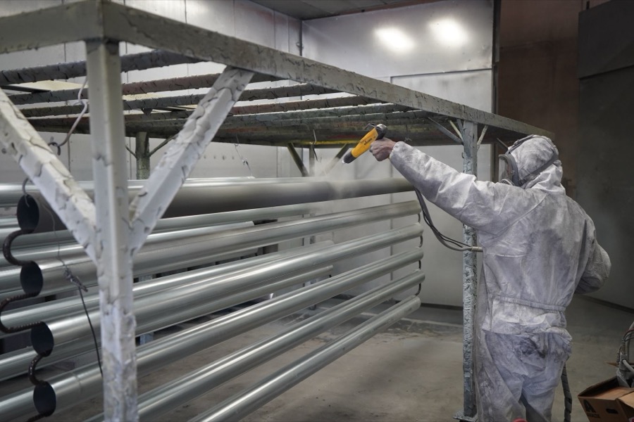 A hand holding a spray gun applying primer to a car body panel during paint repair.