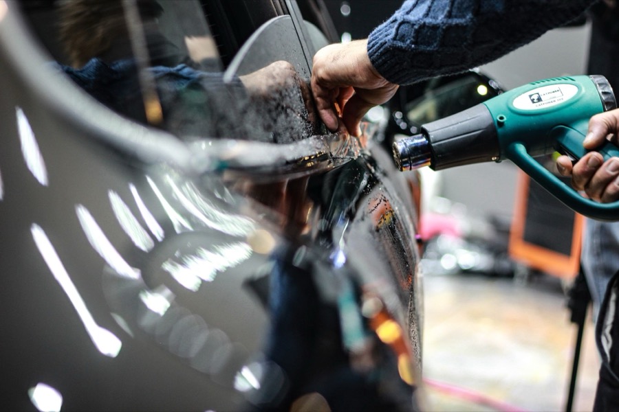Person applying automotive primer to a prepped car body panel.