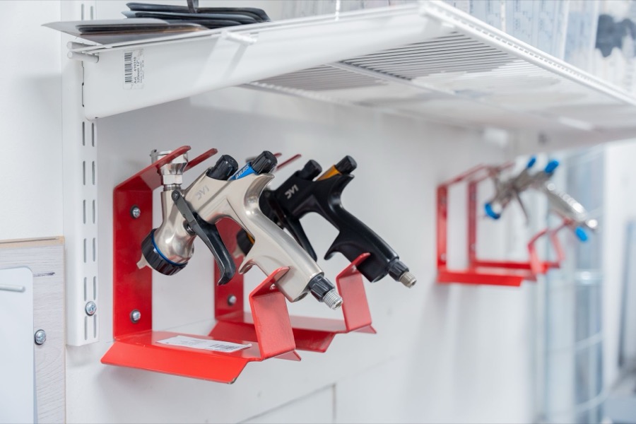 Close-up of a spray gun applying grey primer evenly to a prepped car body panel.