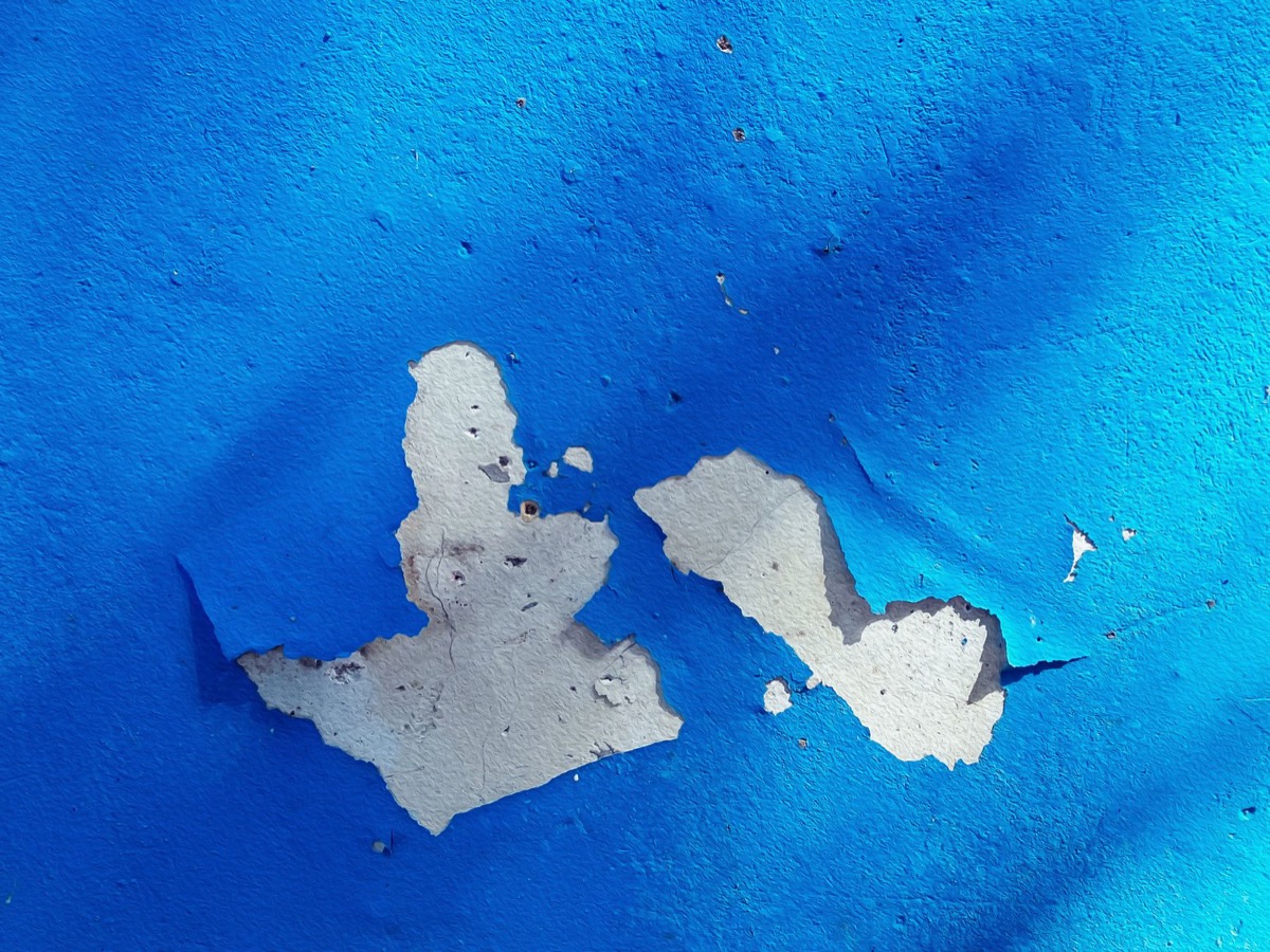 Close-up of interior wall paint with several large bubbles and blisters, indicative of moisture damage or poor adhesion.