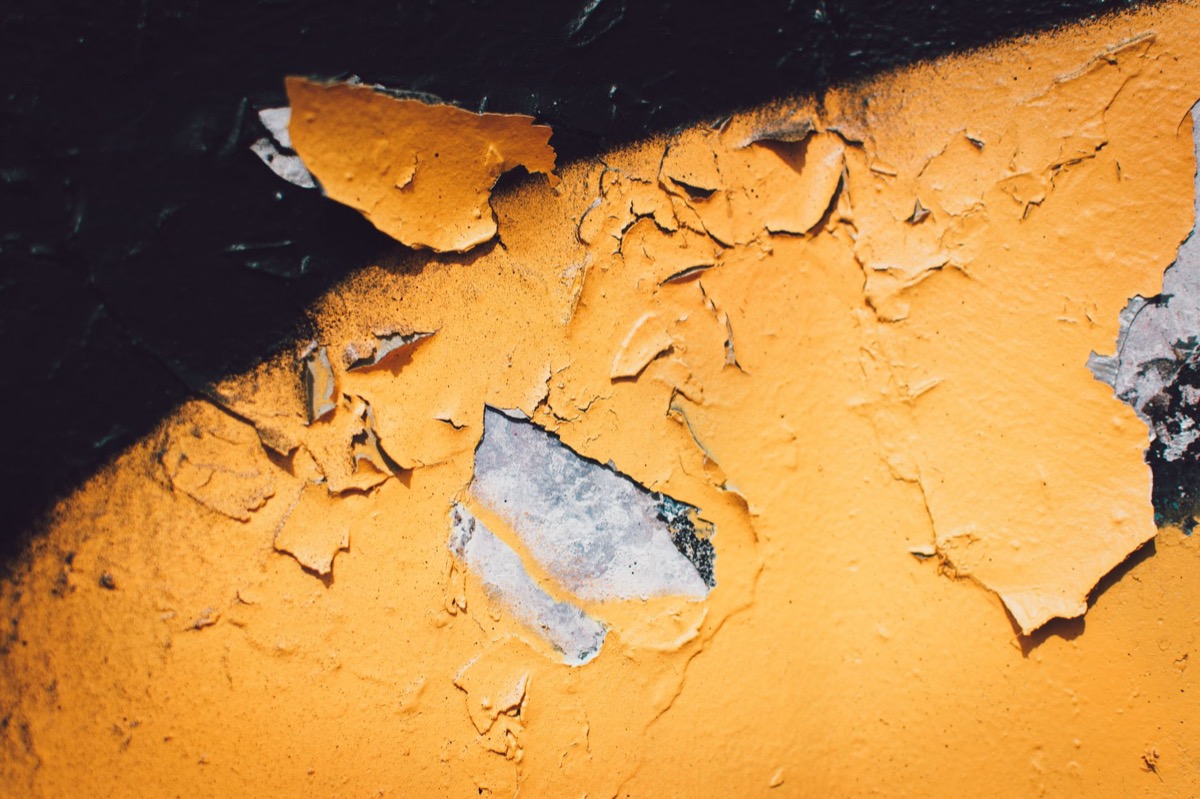 Close-up of paint blistering and peeling on a wall, showing damage and potential moisture issues.