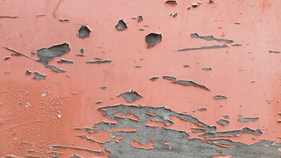 Hand holding a moisture meter against a wall with bubbling paint to check for moisture.