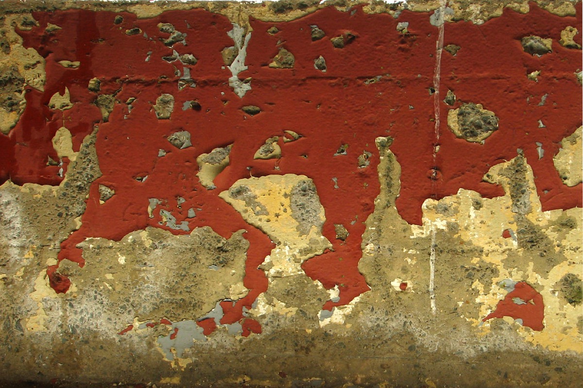 Close-up of a painted wall with significant peeling and flaking, revealing the substrate beneath.