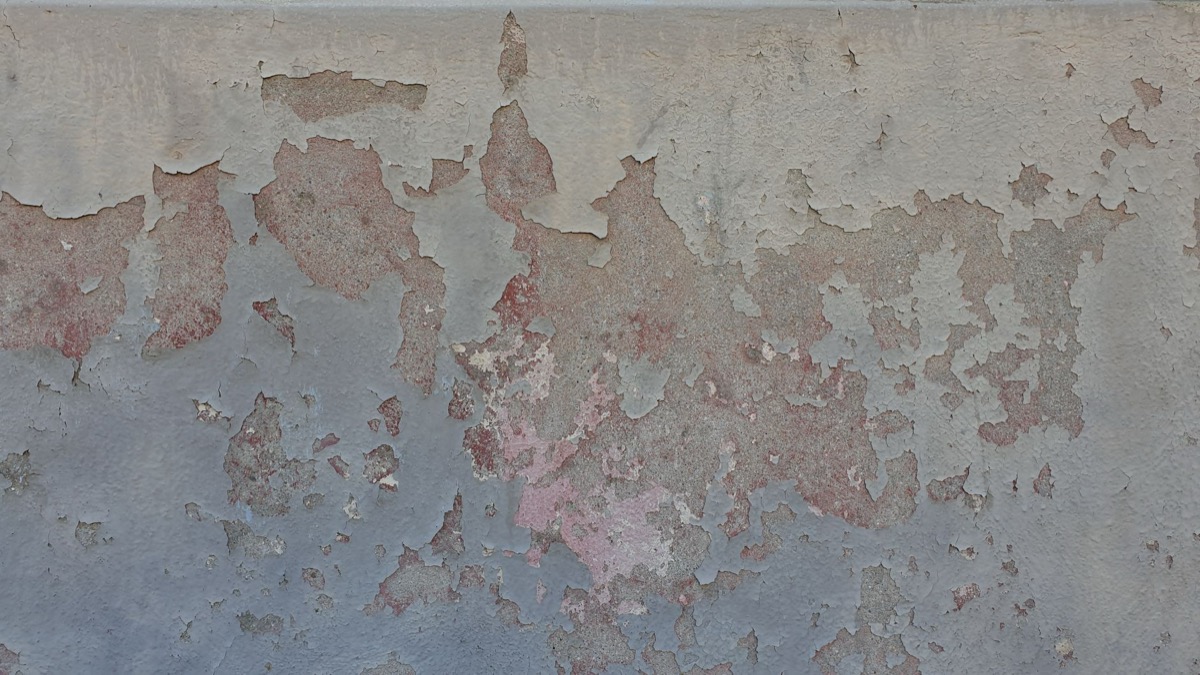 Close-up of severely flaking and peeling white paint on an old wall, revealing damaged plaster underneath.