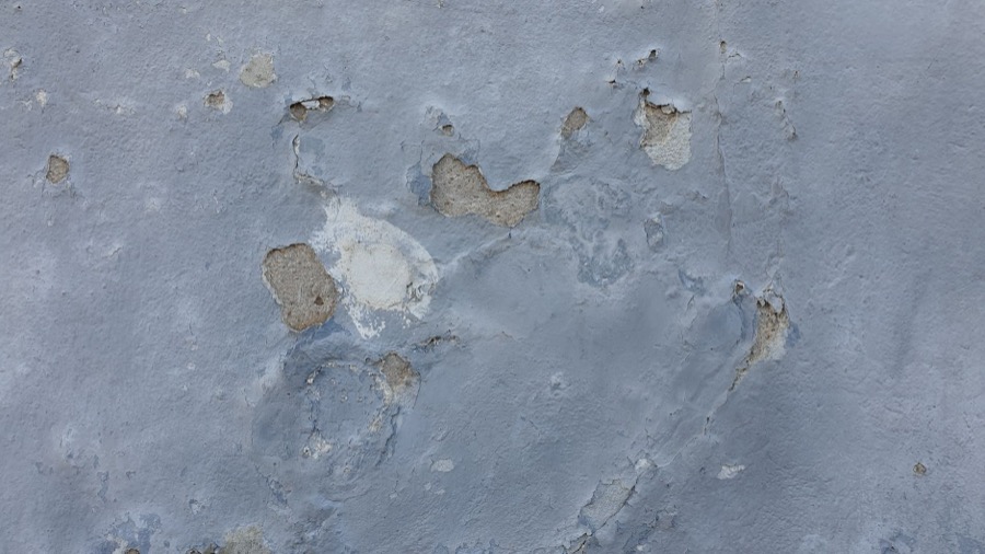 Person using a paint scraper to remove loose, peeling paint from a wall before repainting.